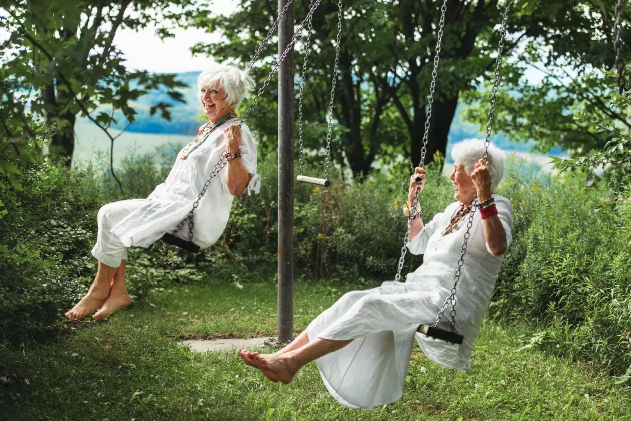 two senior women friends laughing on swing